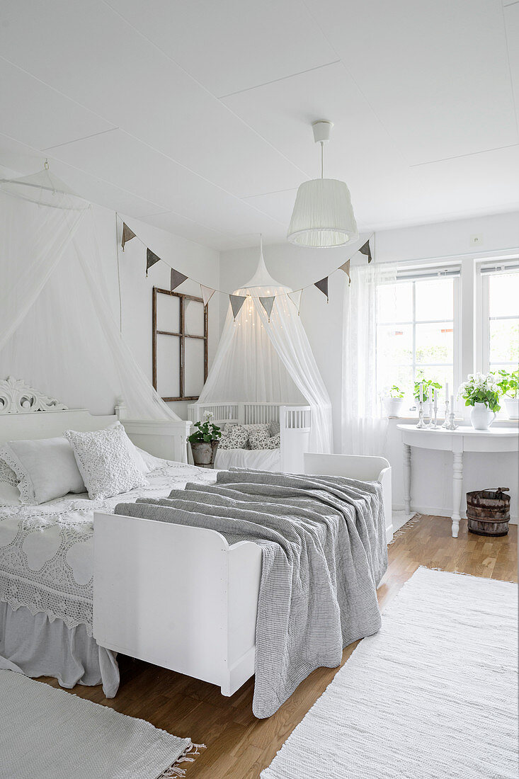 Cot and child's bed in parent's bedroom decorated entirely in white
