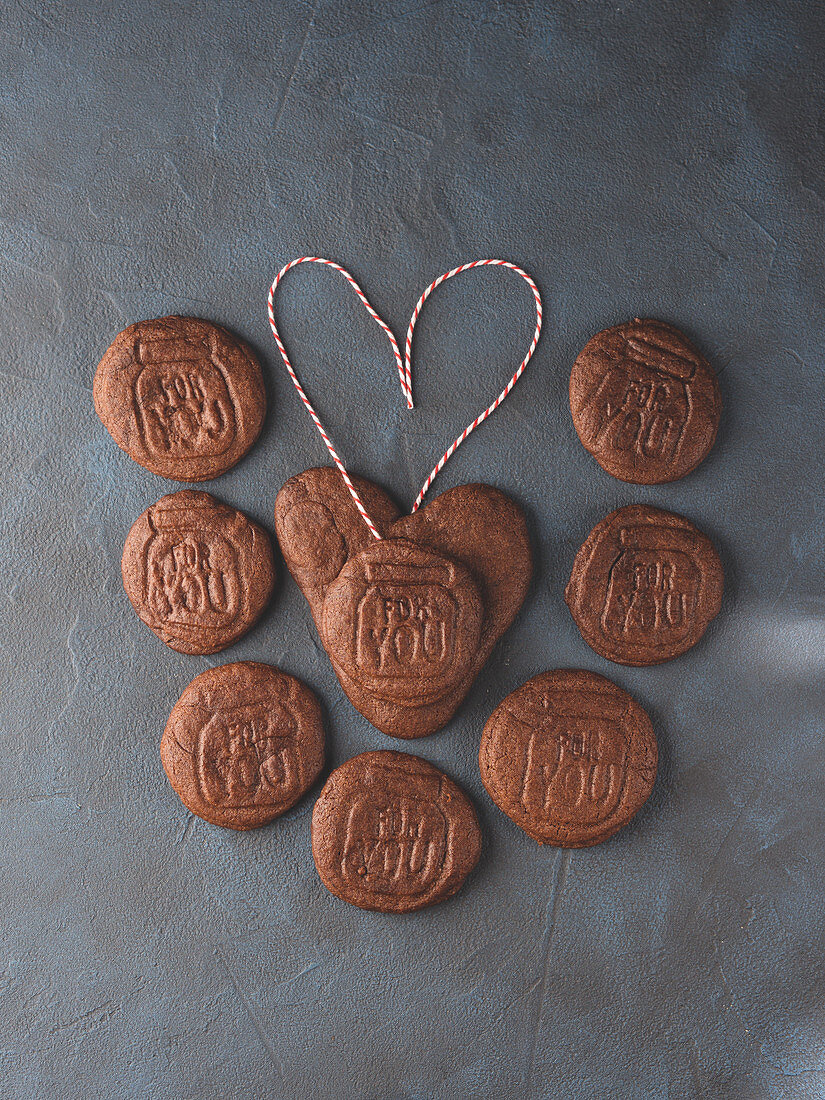 Heart shaped chocolate cookie surrounded by cookies spelling For You over black background