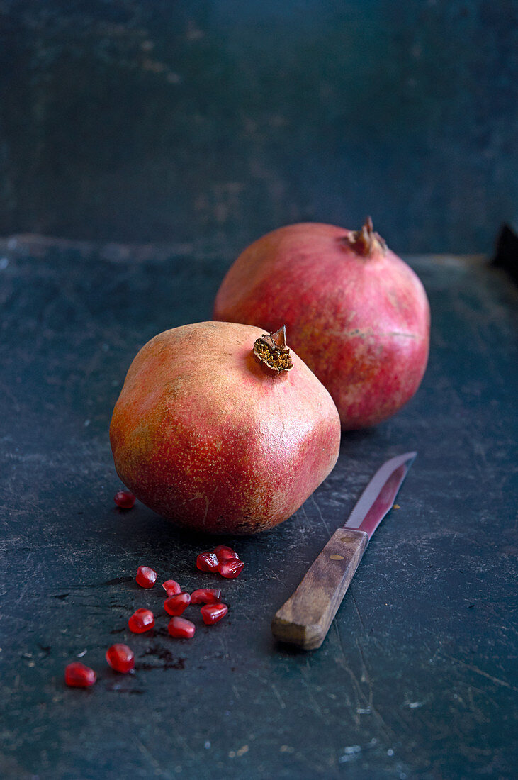 Two pomegranates, pomegranate seeds, and a fruit knife