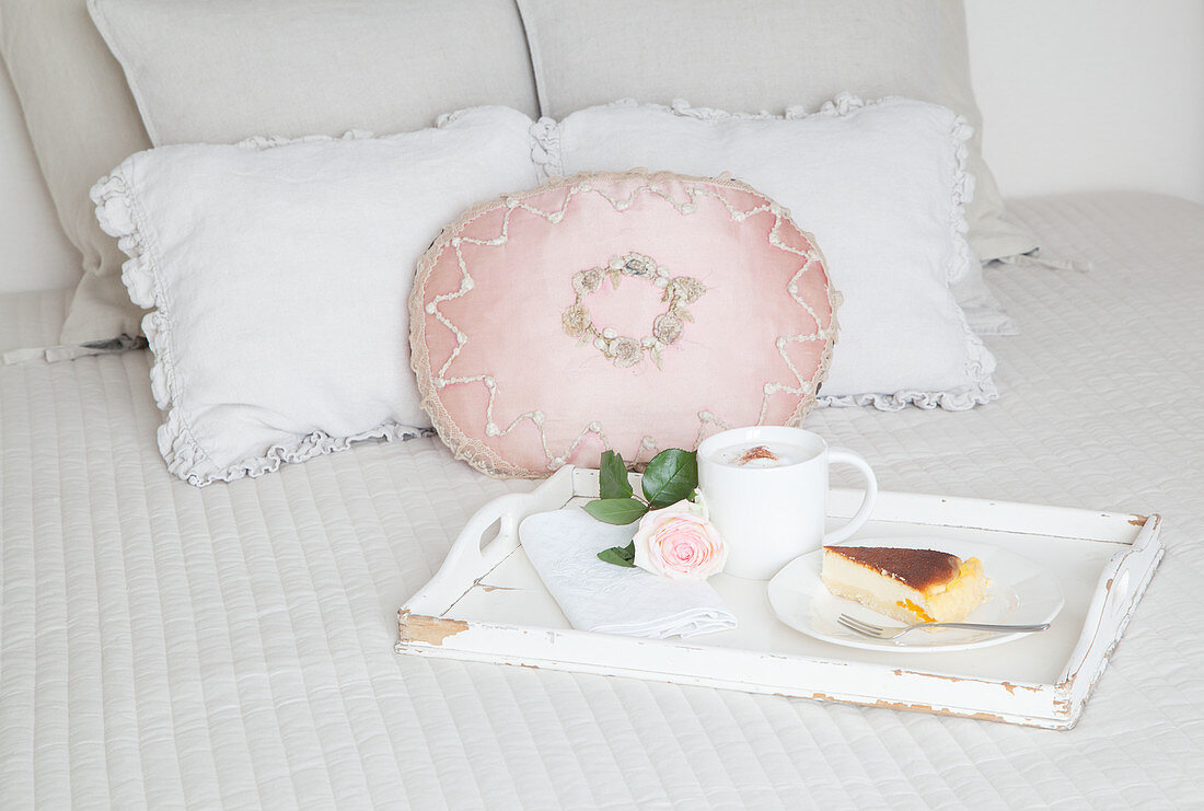 Coffee, cake and a single rose on tray on bed