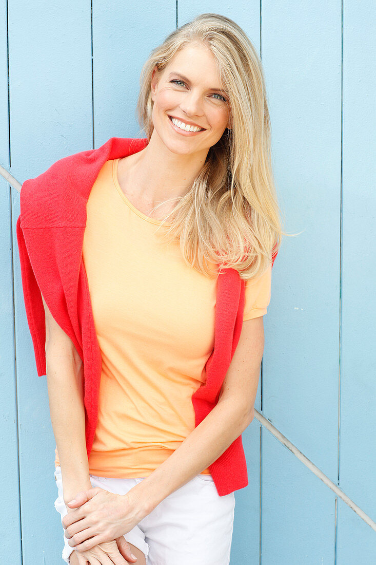 A young blonde woman wearing a yellow t-shirt with a red jumper over her shoulders