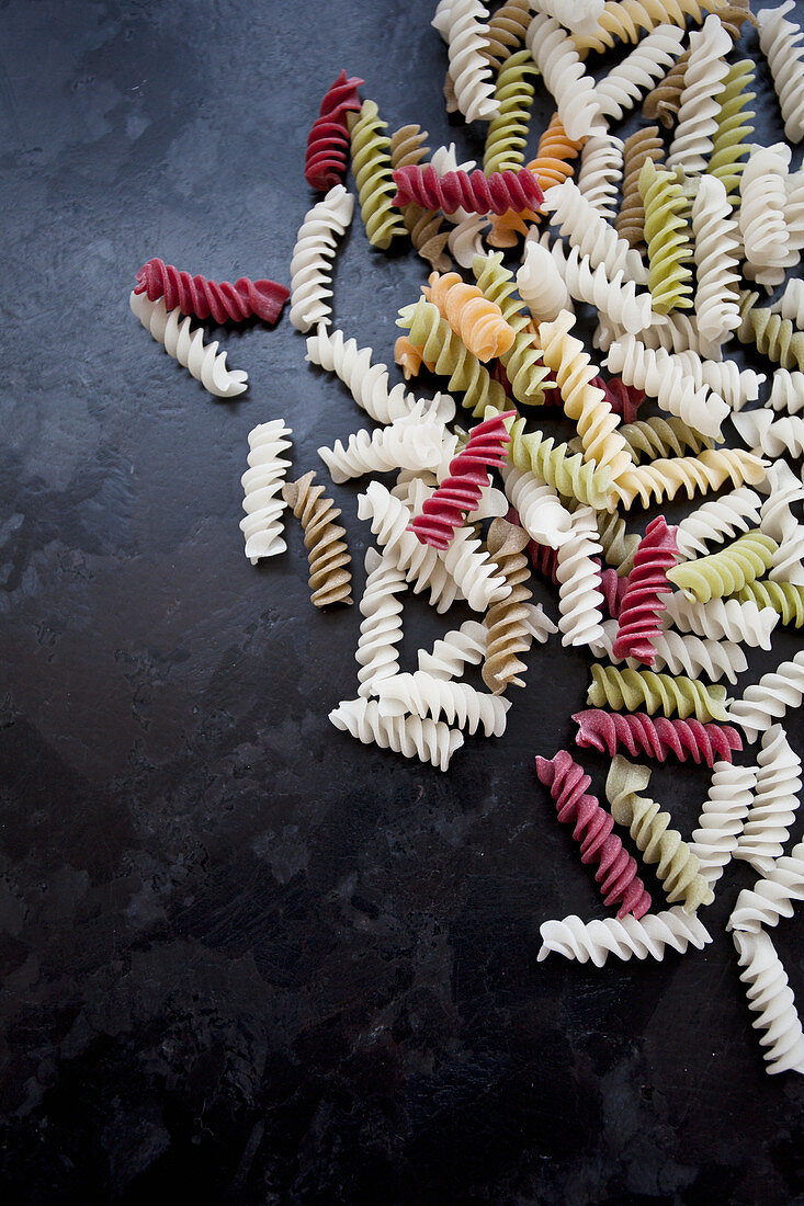 Colourful fusili pasta made from vegetables (beet, spinach), on a black countertop