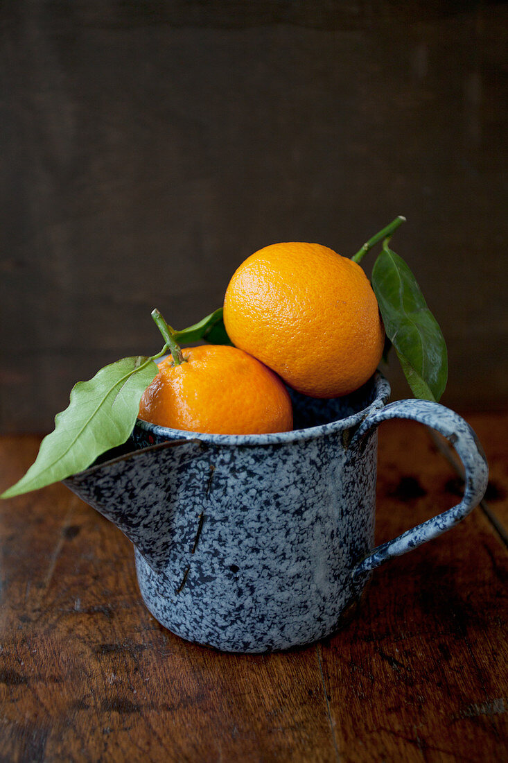 Two oranges in an antique blue enamel jug, sitting on a wooden tabletop