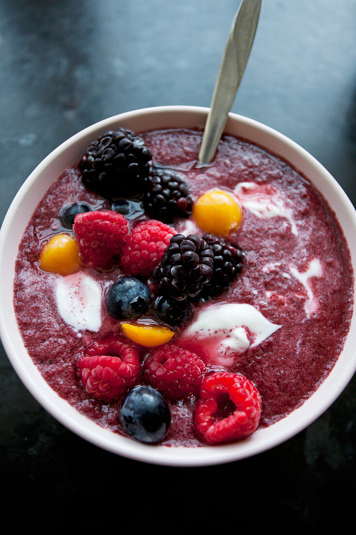 A purple berry smoothie bowl topped with yogurt and frozen blackberries, blueberries, raspberries and golden berries