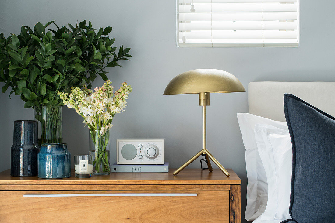 Golden table lamp, radio and vases of flowers and leaves on bedside table