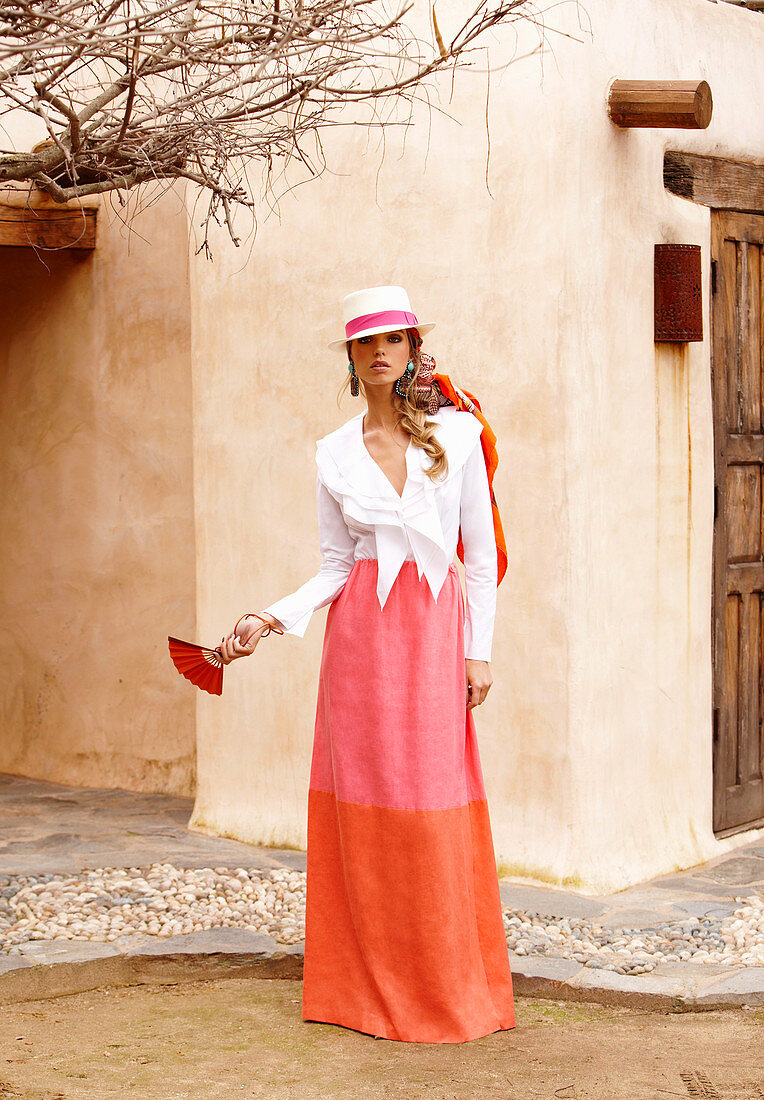A woman wearing a hat, an elegant white blouse and a pink-and-orange maxi skirt