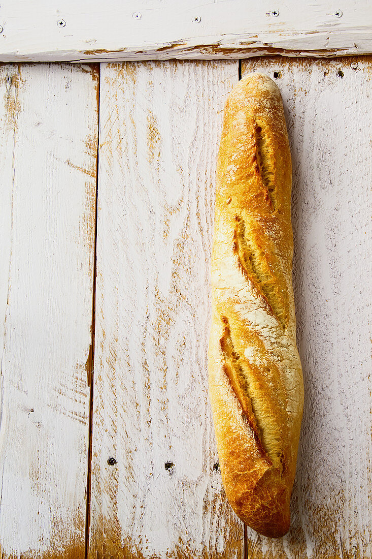 A fresh baguette on a white wooden background (top view)