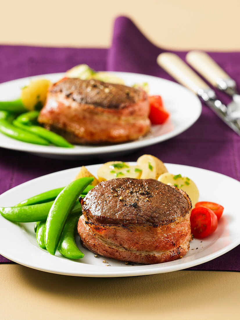 Bacon-wrapped fillet mignons of beef served wtih snap peas, boiled potatoes and cherry tomatoes