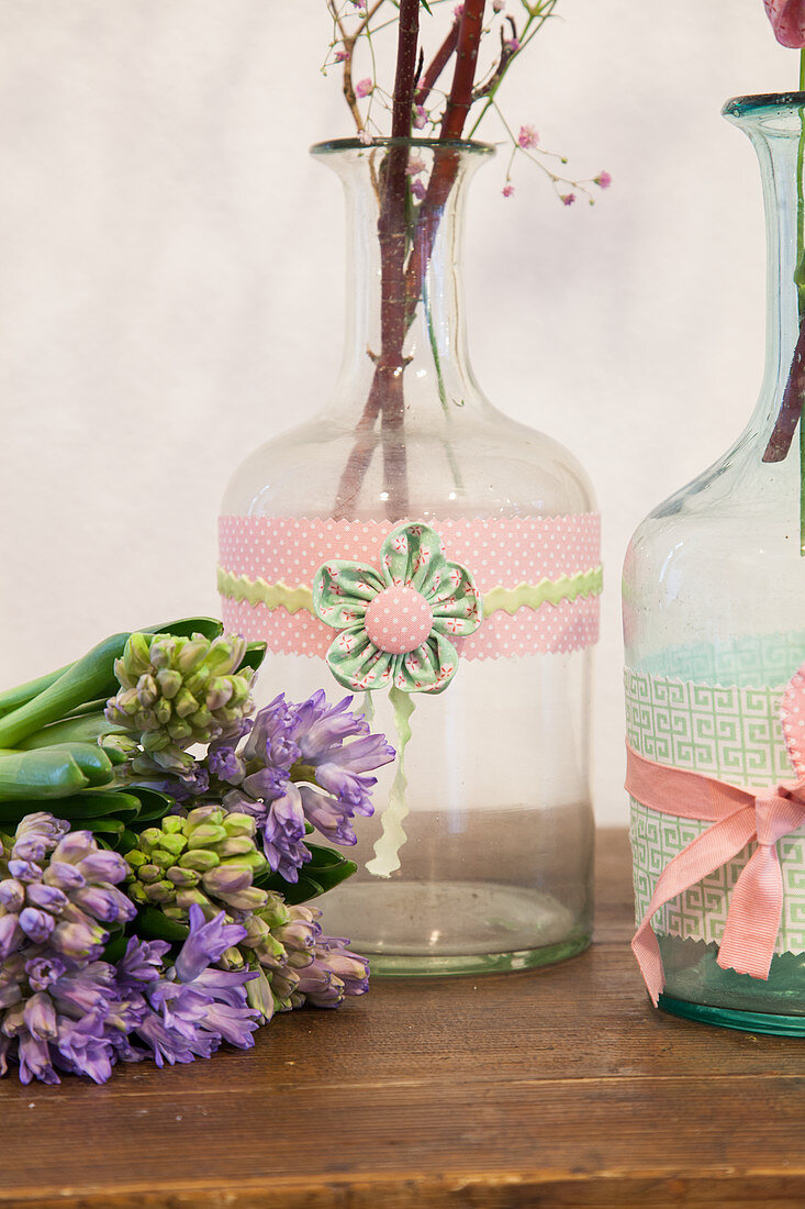 Hyazinthen neben Flaschen mit Borten und Blumen aus Stoff