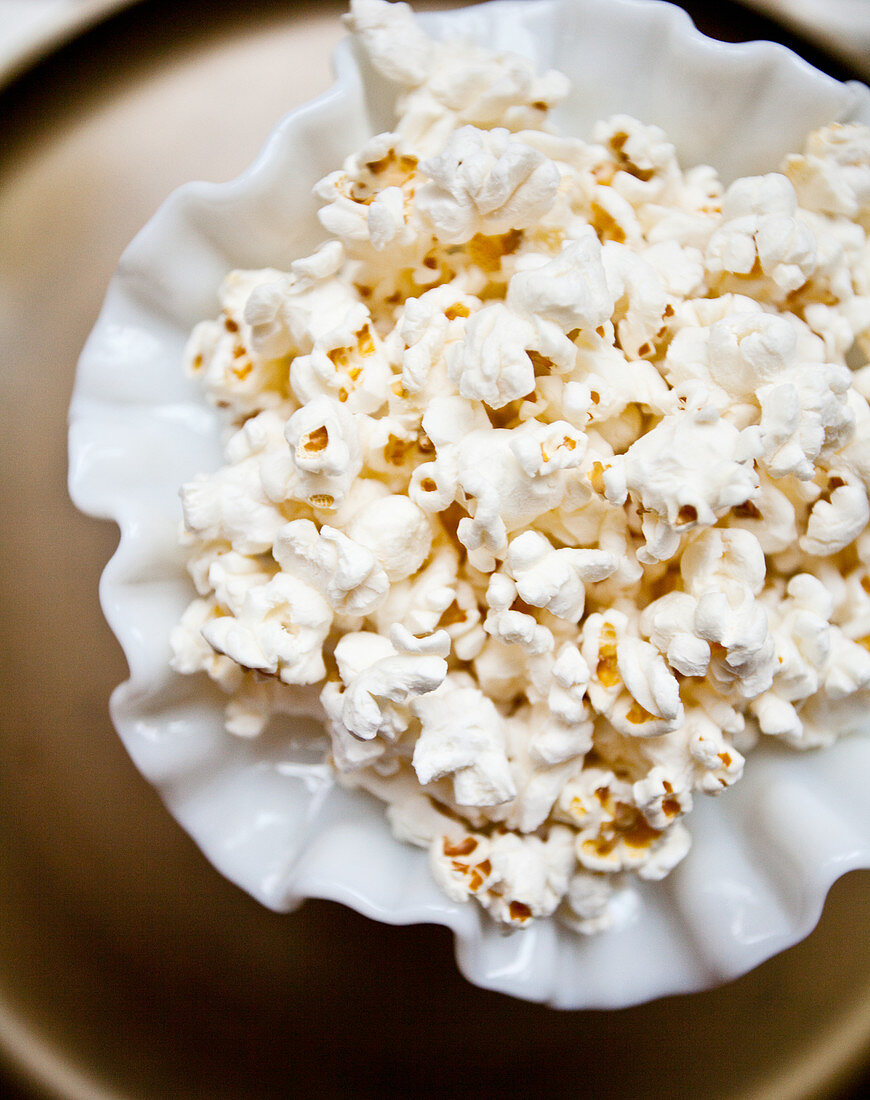 Plain popcorn in an antique white dish, on a gold tray table