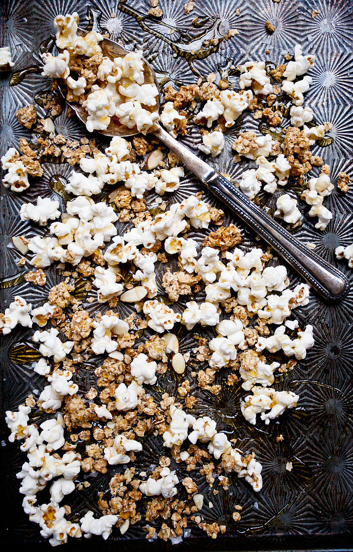 Popcorn as a healthy snack - popcorn, granola and sliced almonds drizzled with manuka honey on an antique baking sheet
