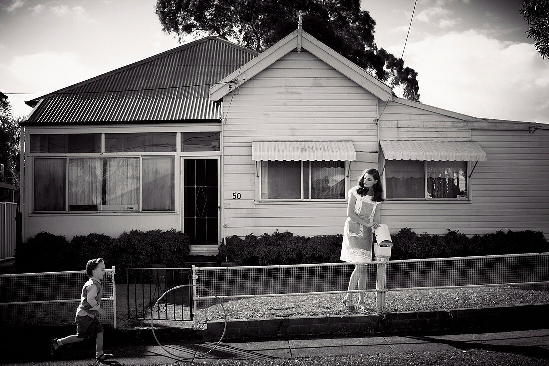 A young woman by a mail box outside a house with a little boy on the pavement (black-and-white shot)