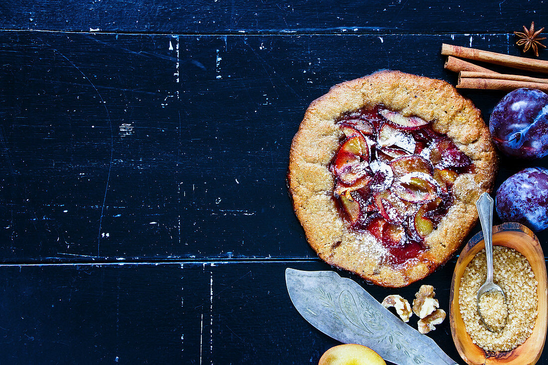 Homemade wholegrain plum pie or tart with walnuts and fresh plums on vintage wooden background
