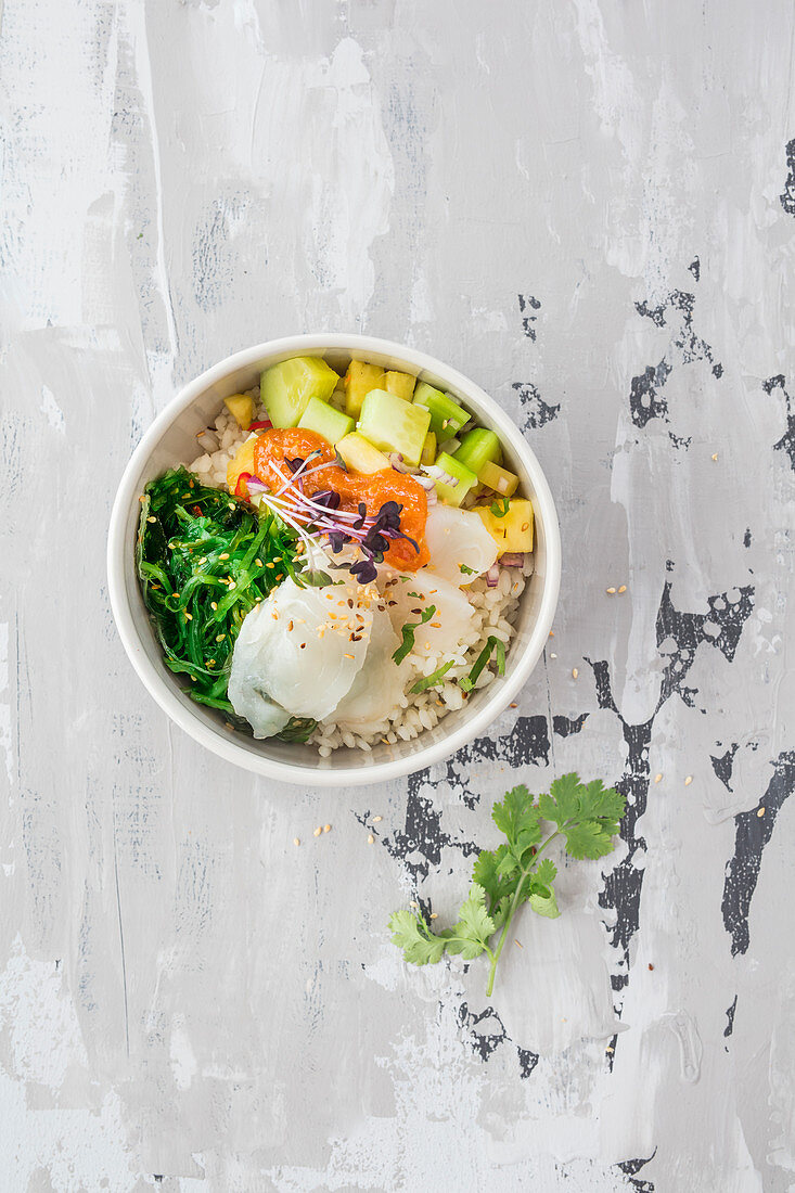 Poke bowl with black halibut, sushi rice, marinated algae and pineapple and cucumber salad served with sukiyaki sauce and sesame seeds (Hawaii)