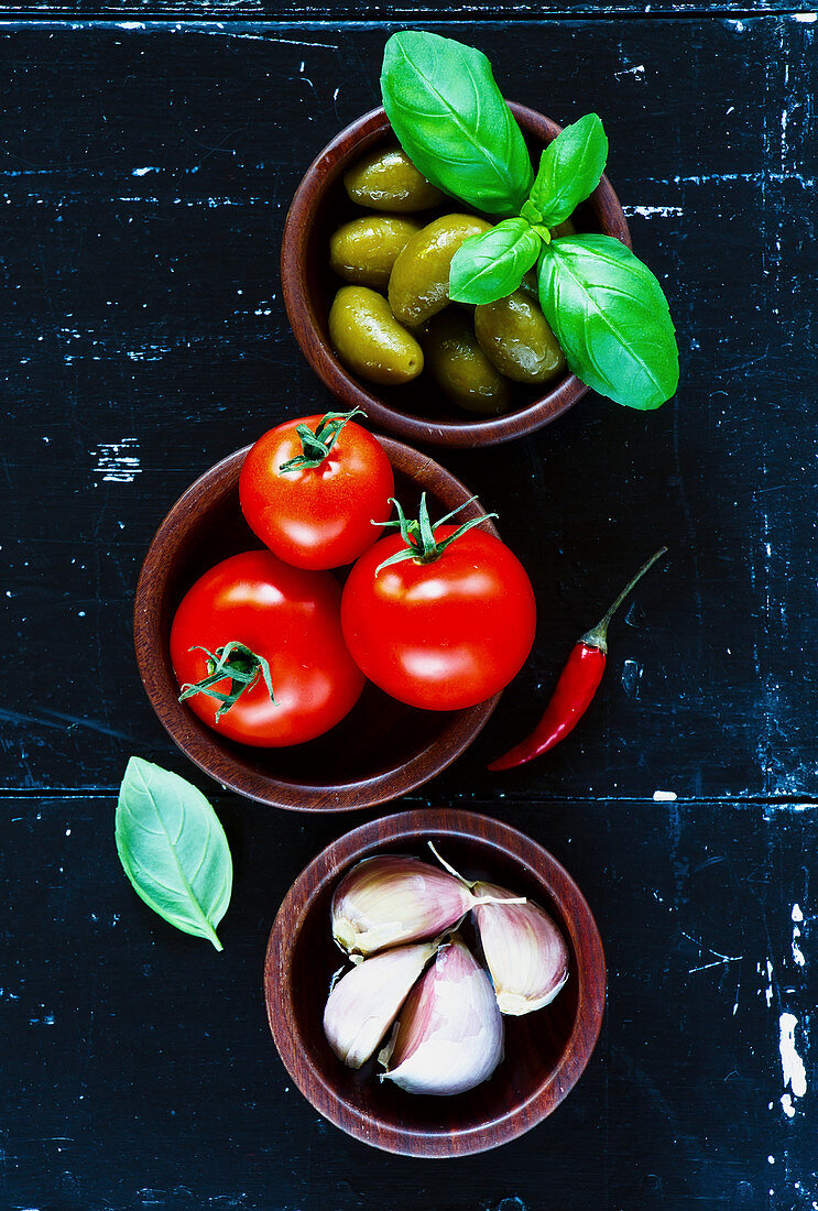 Wooden bowls with green olives, cherry tomatoes and garlic on dark vintage background