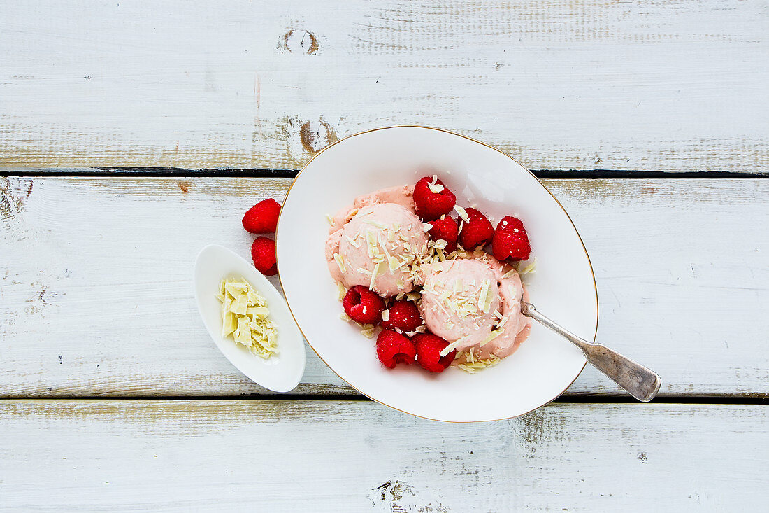 Bowl of organic melting raspberry ice-cream with fresh berries and white chocolate on wooden background