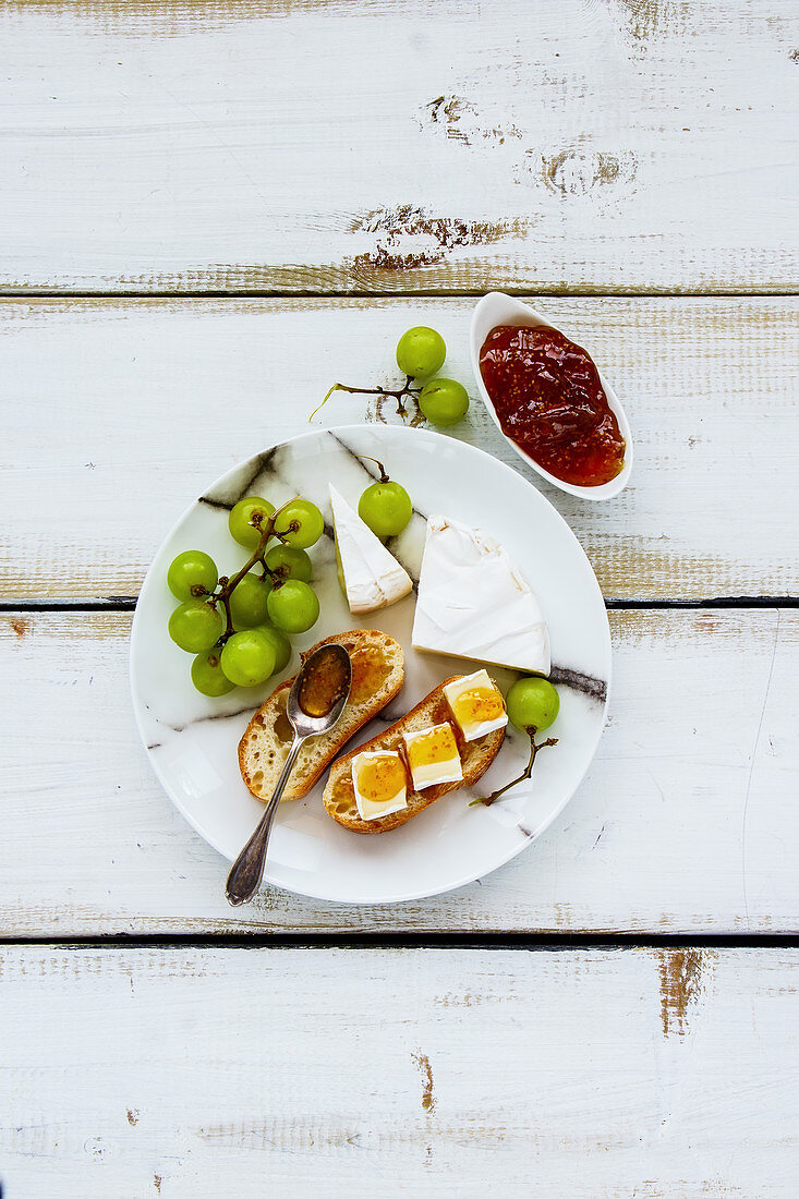 Tasty breakfast set on white wooden table. Brie cheese and fig jam sandwiches with fresh grapes over rustic background