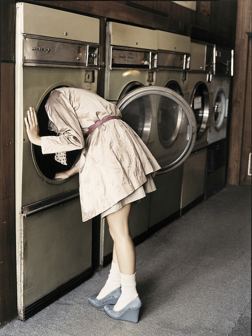 Junge Frau in hellem Trenchcoat an der Waschmaschine im Waschsalon