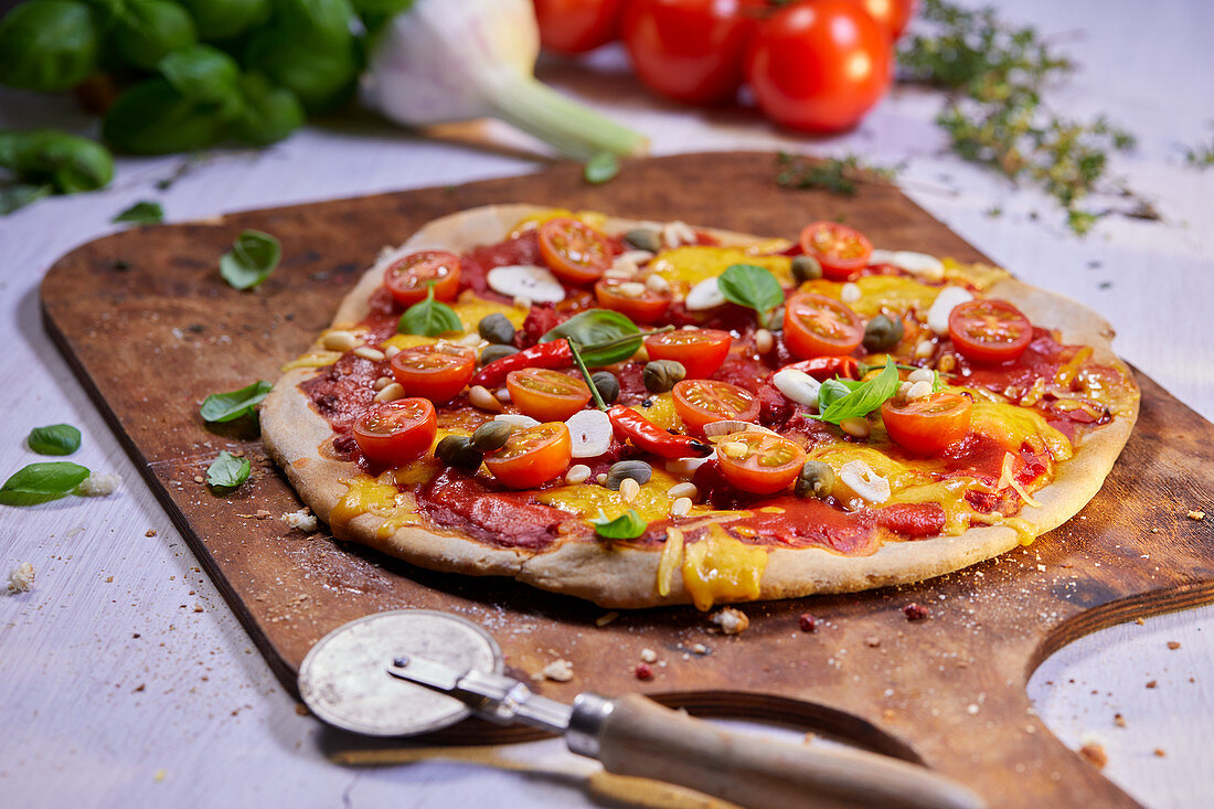 Gemüsepizza mit Tomaten, Chili und Kapern auf Pizzaschieber