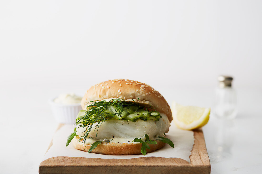 A fish burger with cucumber and dill on a wooden chopping board