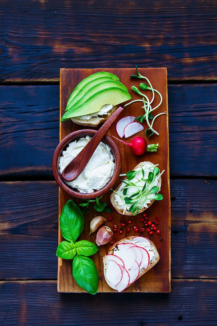 Delicious Sandwiches with avocado, radish, sprouts, cream cheese, herbs and spices, wholegrain bun on rustic wooden board