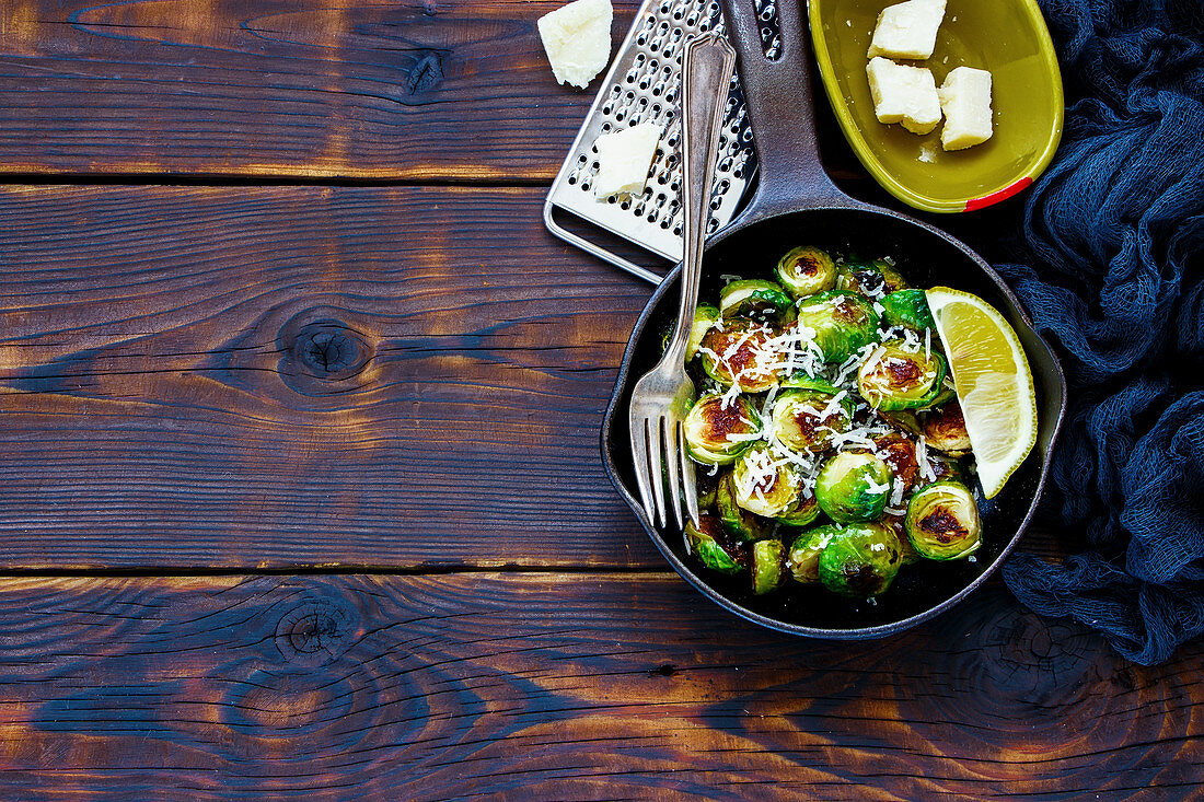 Old cast iron pan of roasted brussels sprouts with cheese parmesan on wooden rustic background