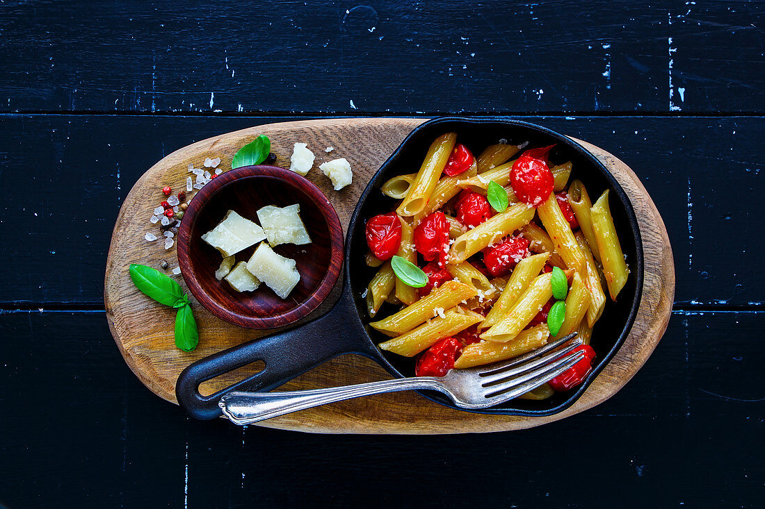 Italian dinner on black rustic wood background. Pasta penne with roasted tomatoes, basil and parmesan cheese