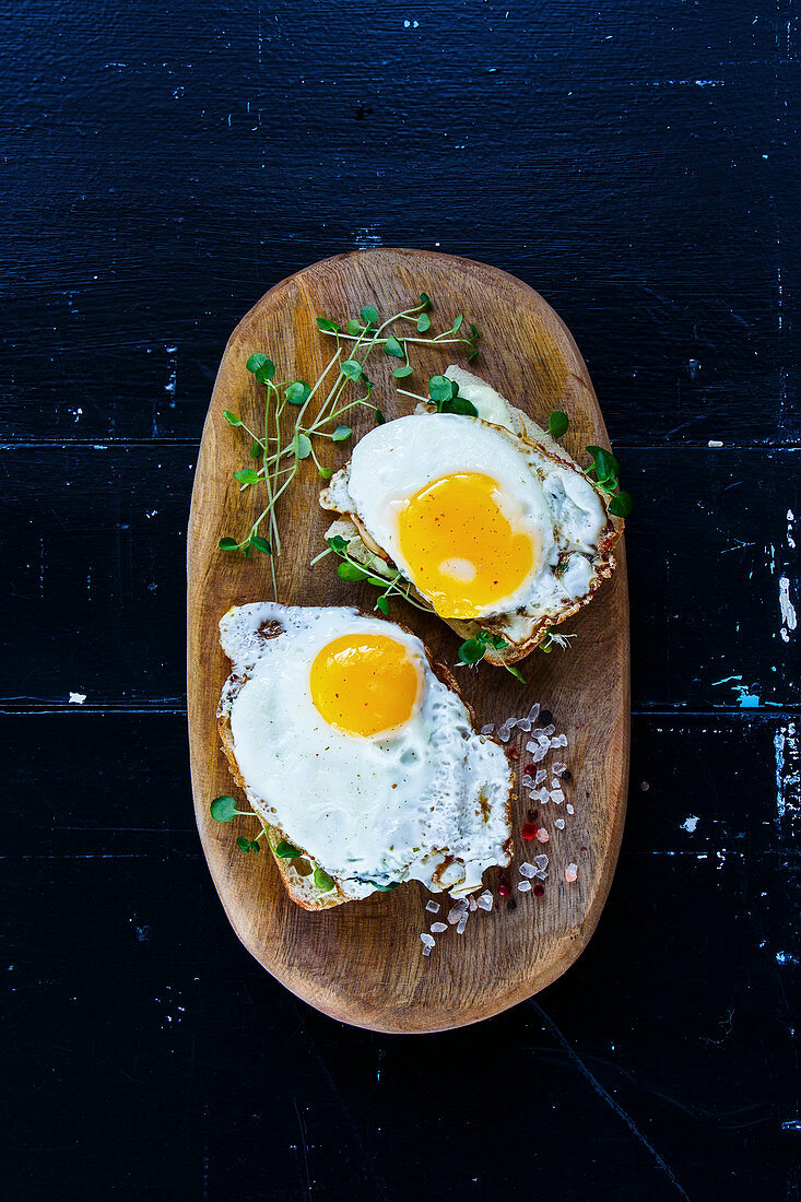 Closen up of breakfast toast with fried eggs and sprouts on wooden board over black grunge background