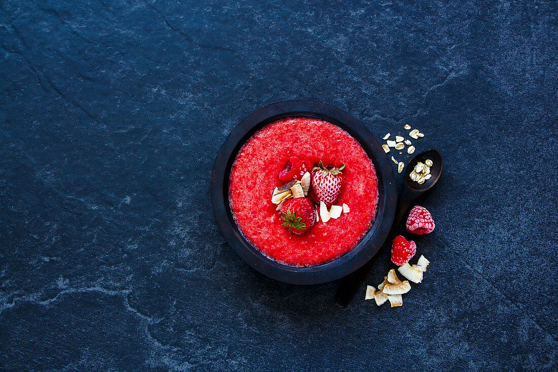 Vintage wooden bowl of tasty berry detox smoothie with frozen berries and oats over dark concrete background