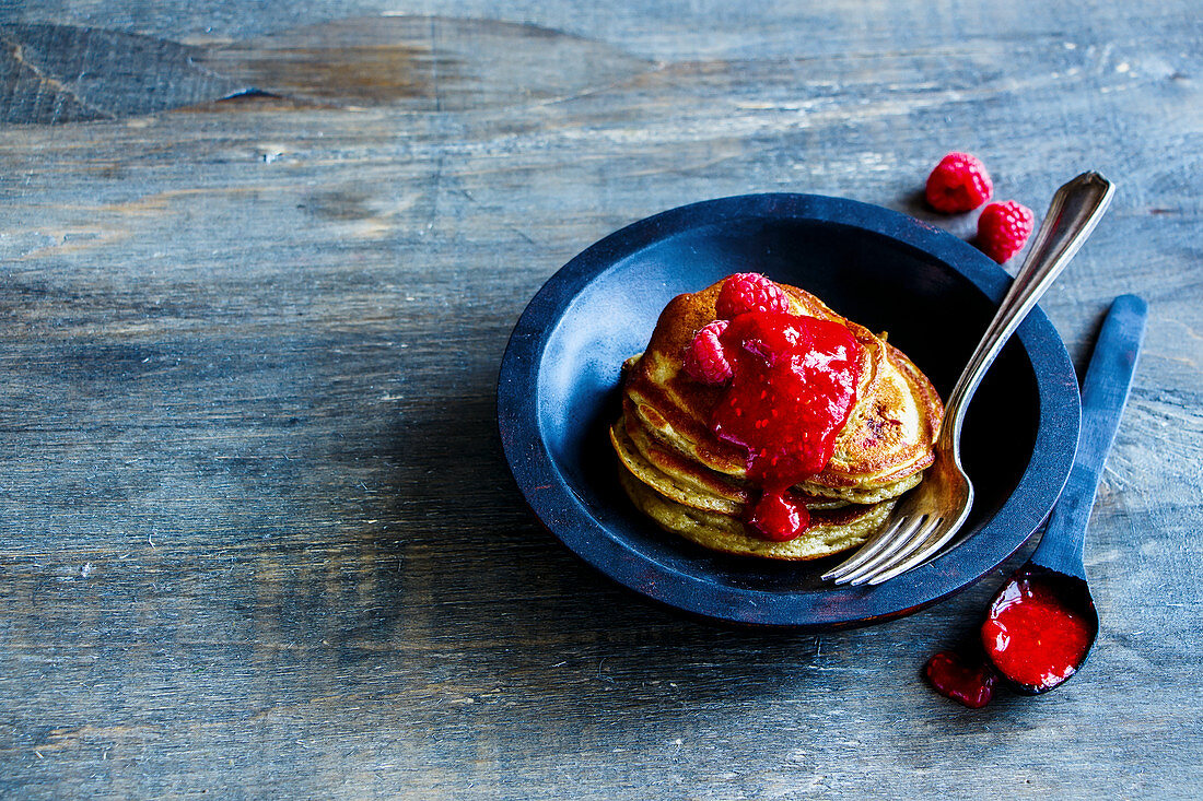 Close up of freshly made pancakes with raspberry jam and fresh raspberries in rustic wooden bowl for breakfast