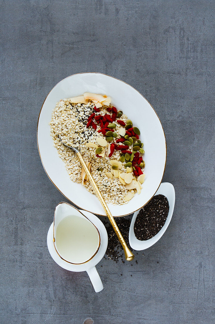 Close up of tasty organic quinoa flakes and healthy breakfast ingredients - milk, coconut flakes, dried fruit, seeds and nuts on grey background