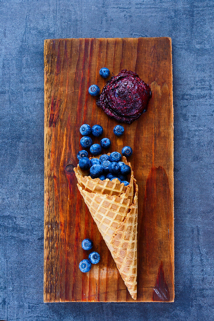Fresh blueberries in waffle cones and homemade sorbet on vintage wooden board over dark stone background