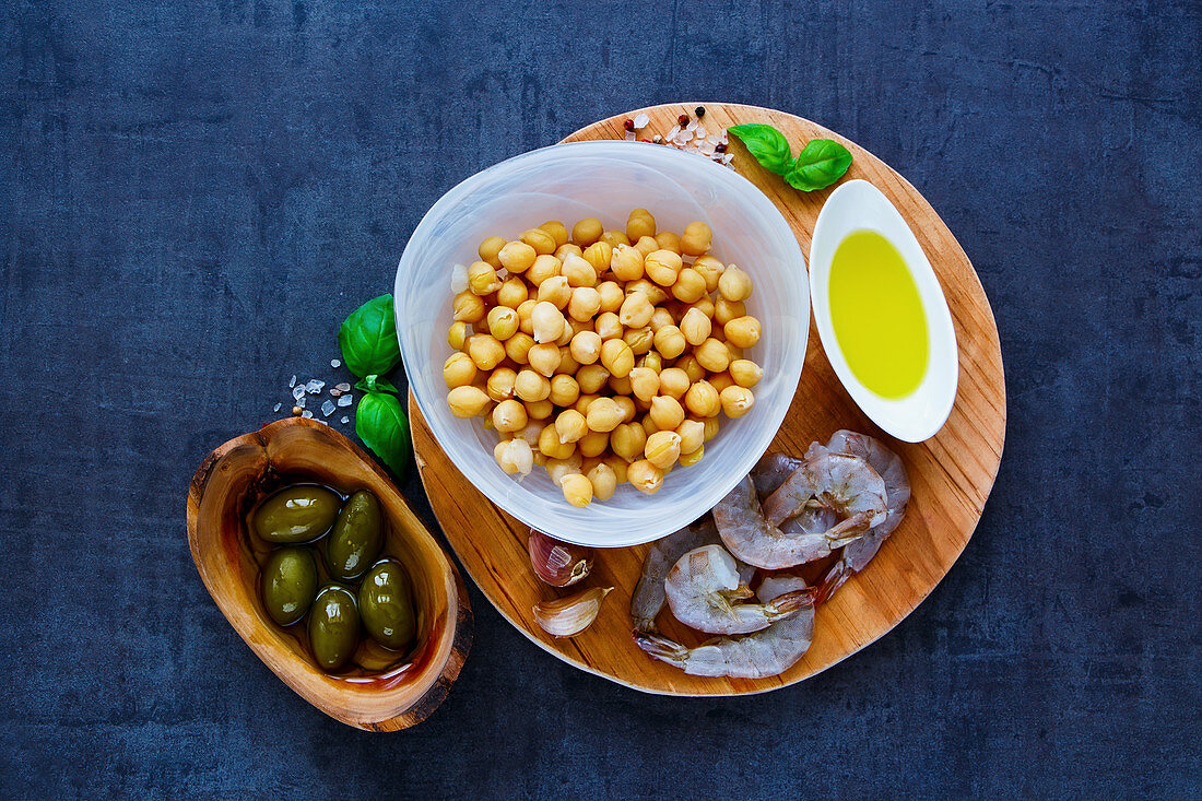 Colorful chickpeas salad ingredients in bowls on round wooden board over dark stone concrete background