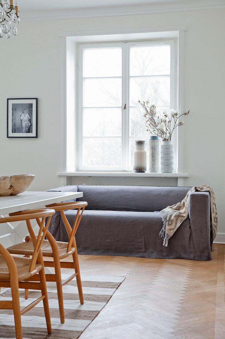 Designerstühle am Esstisch vor dem Sofa mit grauem Überzug