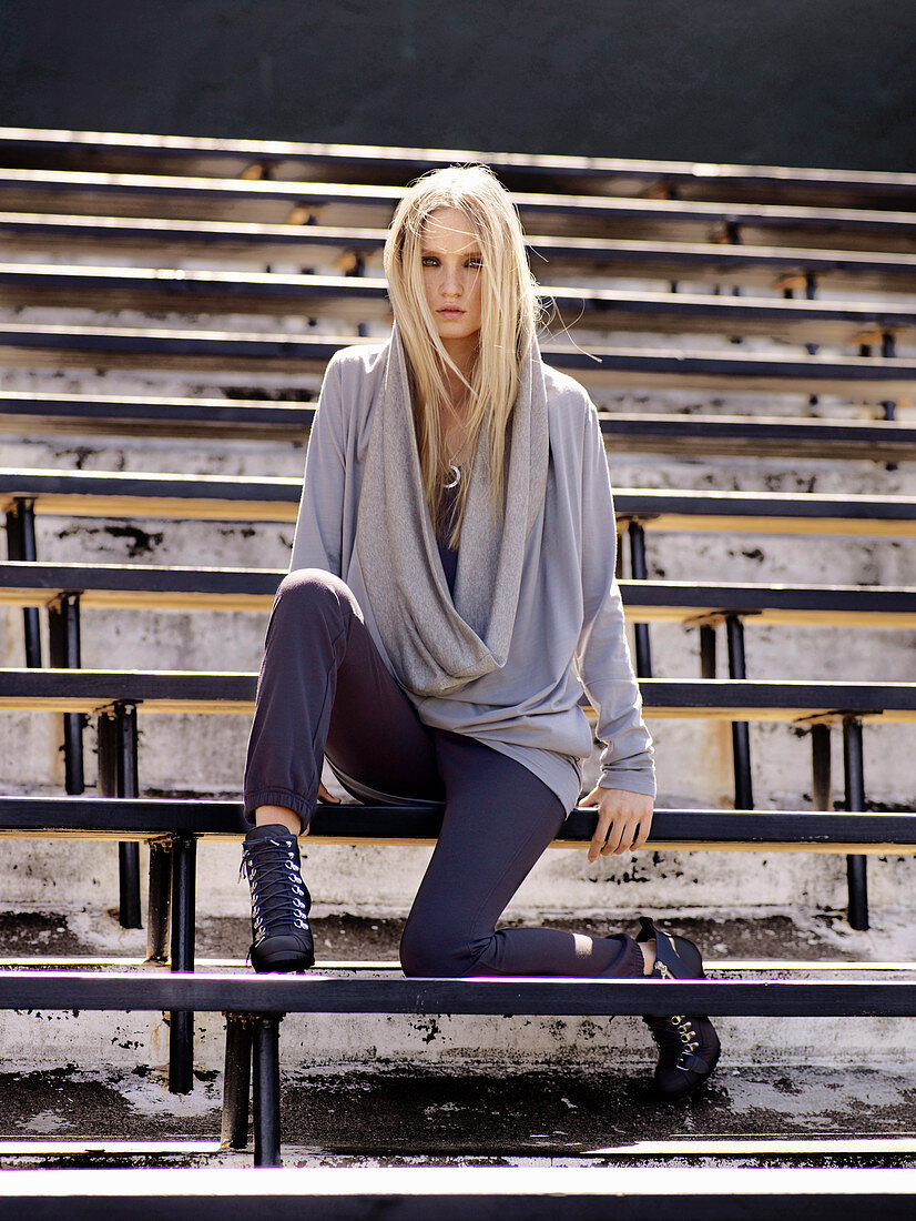 A young woman sitting on a stadium bench wearing a sporty outfit