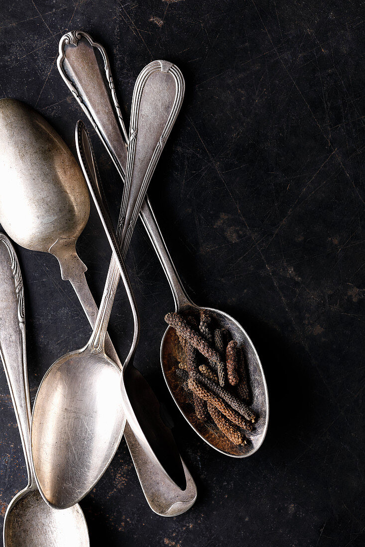 Five silver spoons with pepper on a dark background