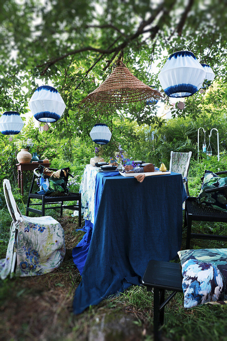 Gedeckter Tisch unter weiß-blauen Laternen im Garten