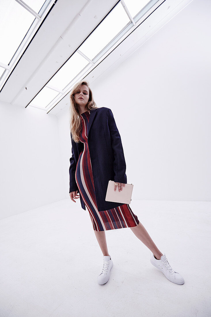 A young woman wearing a striped dress and a dark blue coat