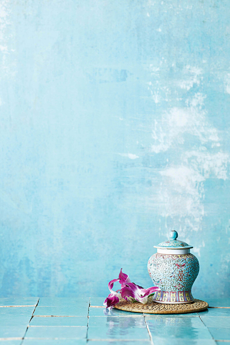 Verziertes asiatisches Porzellangefäss und Orchideenblüten vor blauem Hintergrund