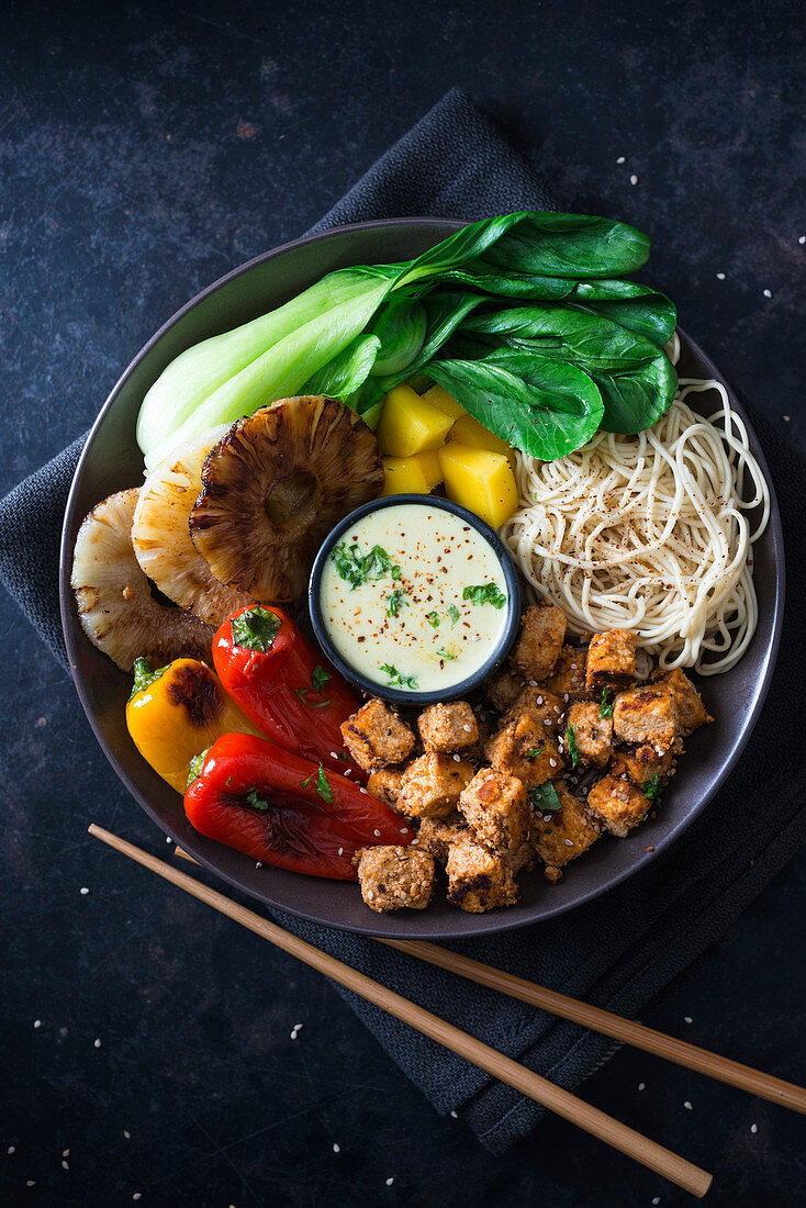 Vegane Buddha-Bowl mit Mie-Nudeln, Mango, Ananas, Pak Choi, gegrillter Paprika, Tofu und Kokos-Curry-Sauce (Asien)