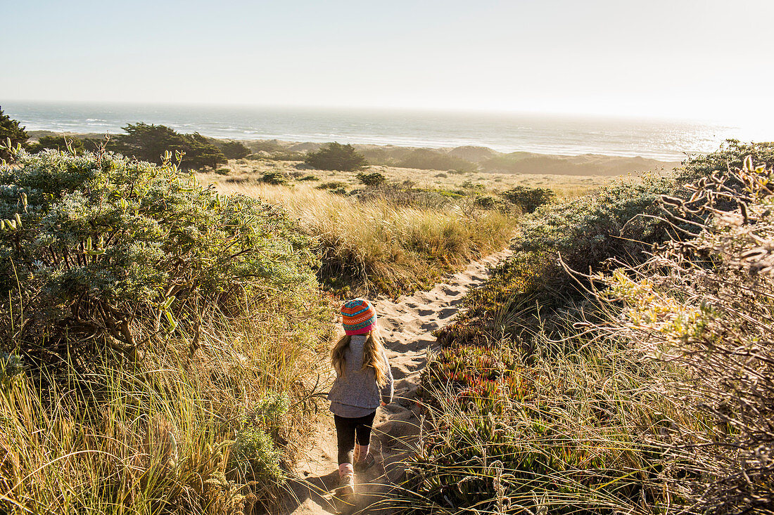 Kleines Mädchen geht auf Sandweg Richtung Meer