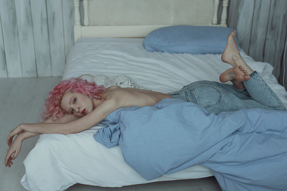 Junge Frau mit rosa Haaren in Jeans und oben ohne liegt auf dem Bett