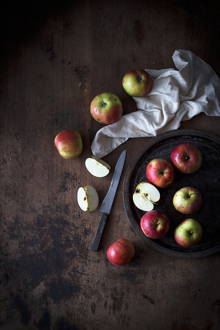 Äpfel auf Teller und dunklem Holzuntergrund (Aufsicht)