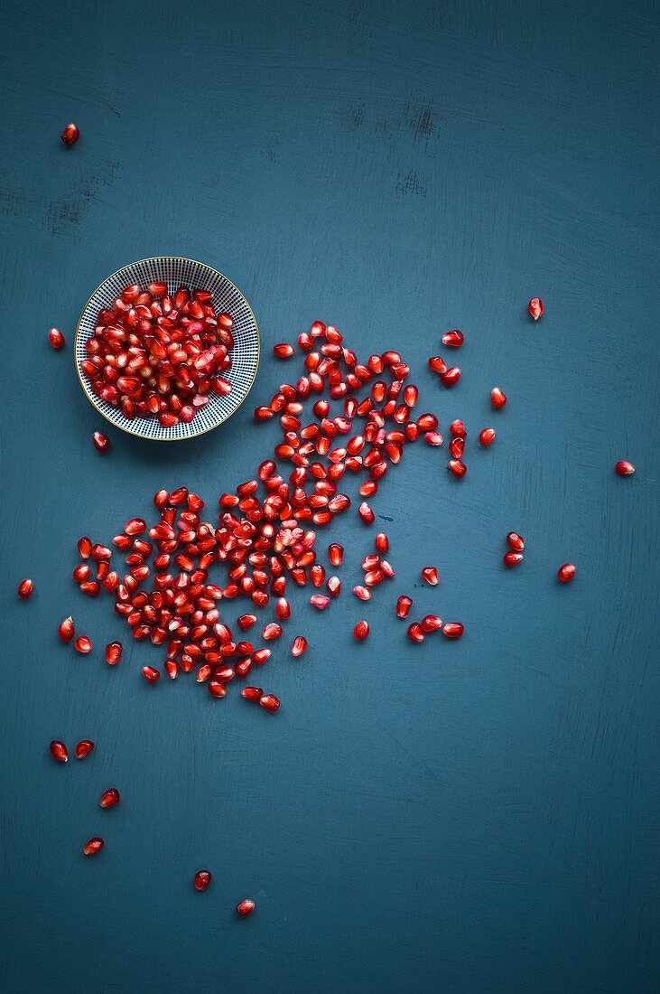 Many pomegranate seeds in a bowl and on a blue background (top view)