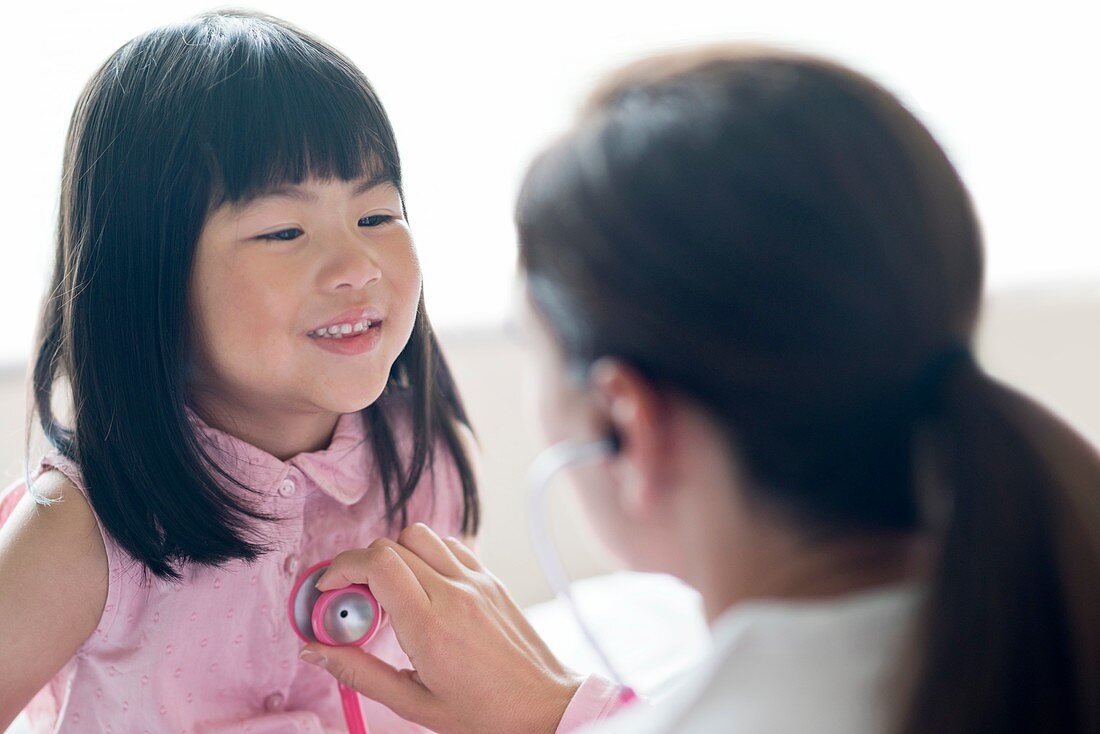 Girl smiling towards nurse using stethoscope