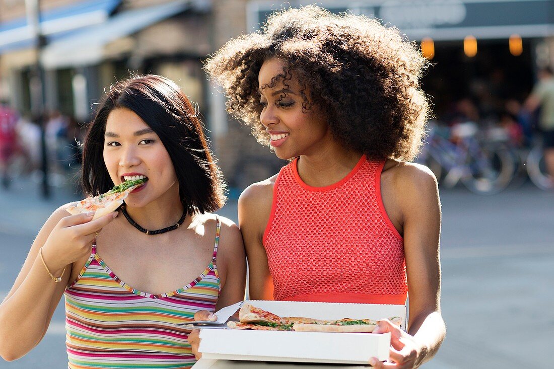 Women eating pizza from box outdoors