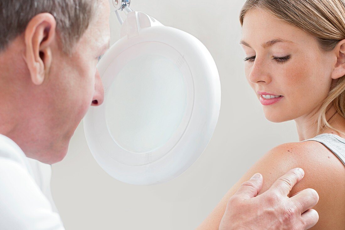 Doctor examining mole on young woman's shoulder