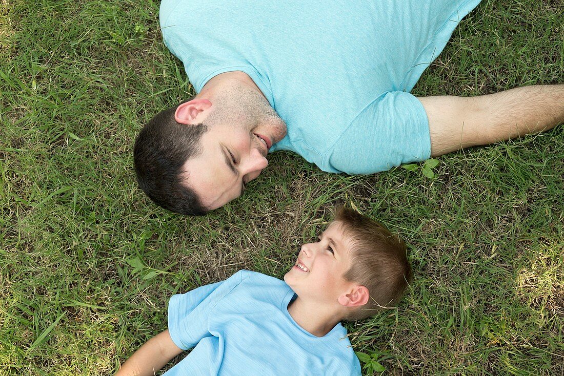 Father and son lying on grass, high angle