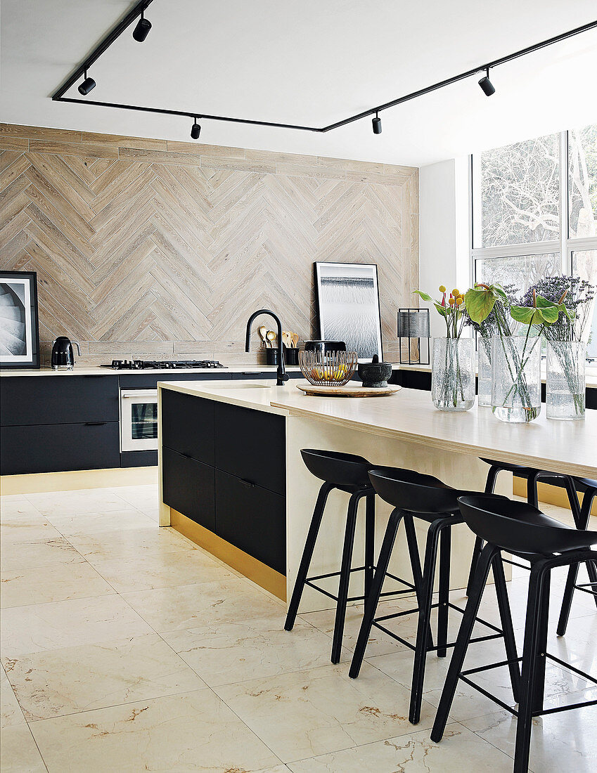 Black cupboards, black bar stools and island counter with extended worksurface in elegant kitchen