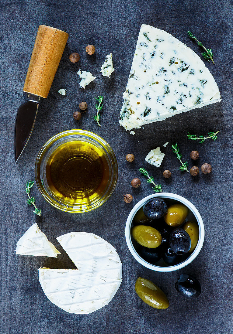 Healthy food background with cheese variety, olive oil, olives and fresh herbs over dark vintage texture